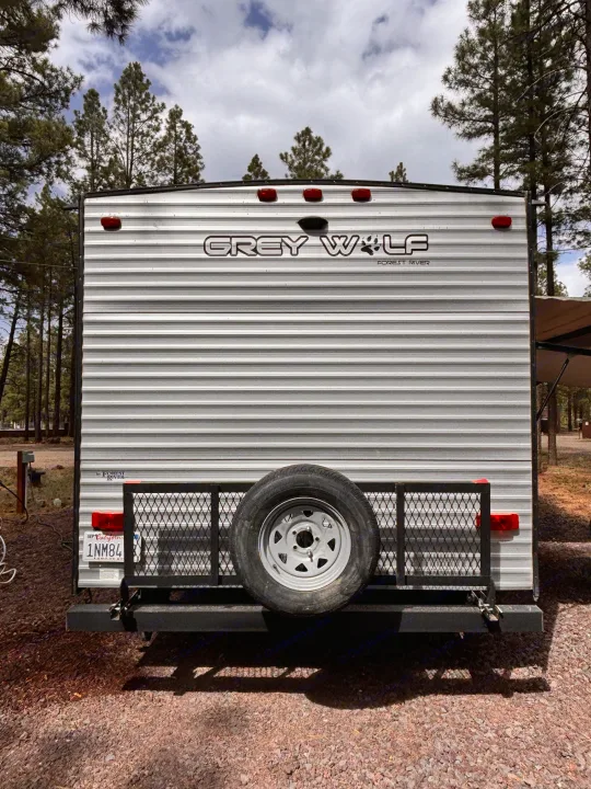 Grey Wolf RV rental: Rear view of a travel trailer with a spare tire, California plate 1NM84, parked in a pine forest.. Forest River Cherokee Grey Wolf 2021