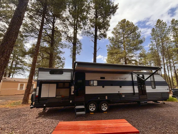 Grey Wolf travel trailer RV rental set in a pine forest campsite. Features an outdoor kitchen and awning, with a picnic table.. Forest River Cherokee Grey Wolf 2021