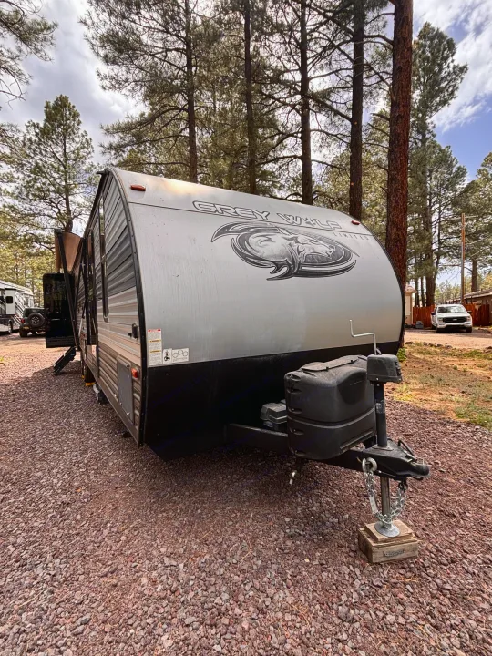 An RV rental travel trailer, a Grey Wolf Limited, parked on gravel in a pine forest, perfect for outdoor trips.. Forest River Cherokee Grey Wolf 2021