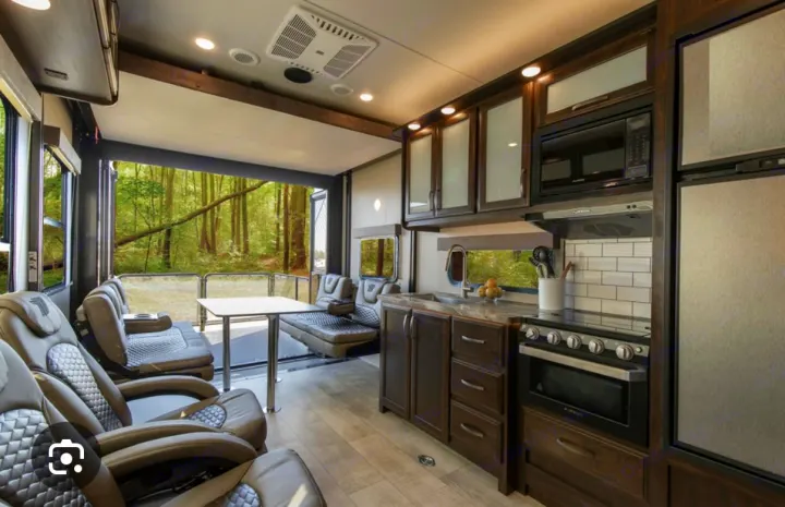 Modern rv rental interior with a fully-equipped kitchen, recliners, and an open rear patio offering a forest view.. Grand Design Momentum 2021