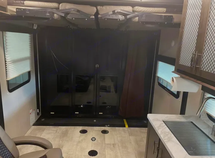 This RV rental interior shows a toy hauler's versatile cargo area with fold-up beds, kitchen counter, and floor tie-downs.. Grand Design Momentum 2021