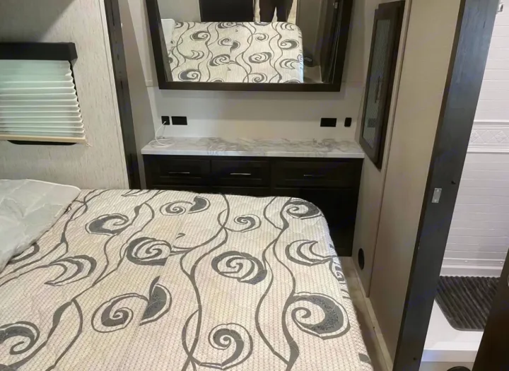RV rental bedroom: comfortable bed, practical storage dresser with mirror, window blinds, and adjacent shower for travel convenience.. Grand Design Momentum 2021
