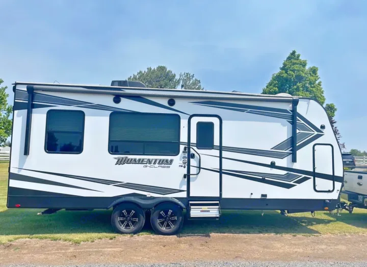 White & black "Momentum G-Class" RV rental with dual axles, parked on grass. This travel trailer is ready for your camping adventures!. Grand Design Momentum 2021