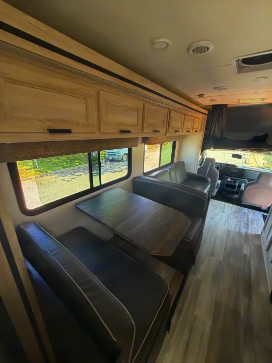 Modern RV rental interior with a light wood dinette, comfortable grey seating, matching table, and wood-look flooring.. Forest River Sunseeker LE 2024