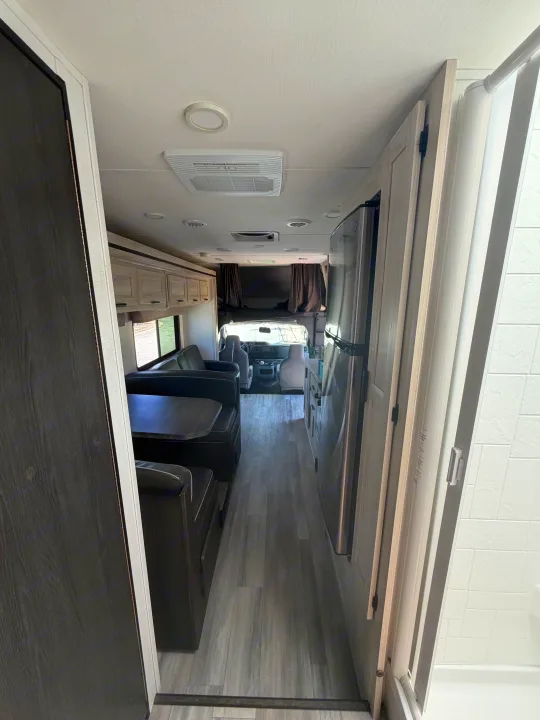 An RV rental interior showing the aisle leading to the dinette, kitchen with fridge, and front driving cabin.. Forest River Sunseeker LE 2024