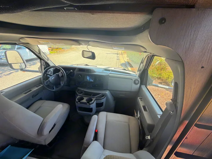 RV rental cab interior with dashboard, steering wheel, front seats, and overhead bunk visible. Ready for adventure!. Forest River Sunseeker LE 2024
