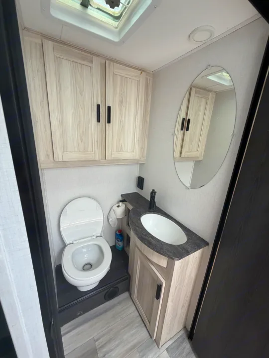 Compact RV rental bathroom with toilet, sink, mirror, and light wood cabinets, featuring a skylight for natural light.. Forest River Sunseeker LE 2024