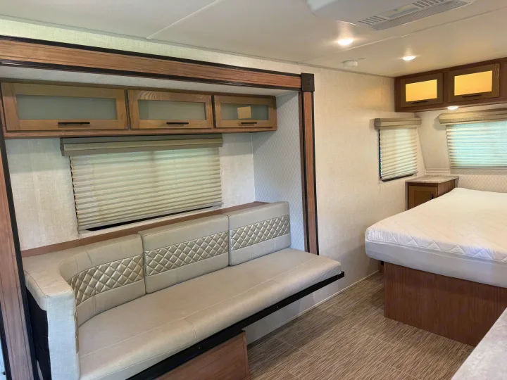 RV rental interior featuring a modern sofa with quilted accents, overhead cabinets, and a comfortable bed for travel.. Forest River R-Pod 2020