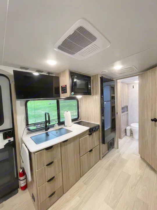 Modern rv rental kitchen with sink, stove, microwave, TV, and view into bathroom. Bright interior for your adventures.. Winnebago M Series 2025