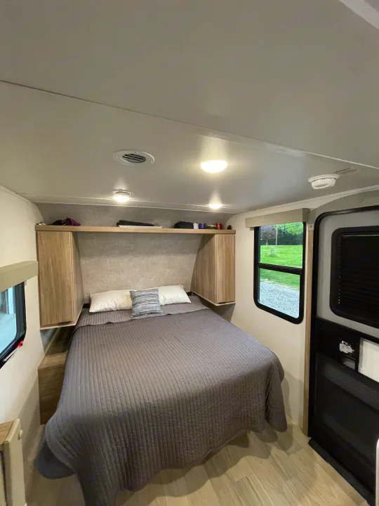 This cozy RV rental bedroom features a comfy bed with gray bedding, overhead storage, and windows offering natural light.. Winnebago M Series 2025