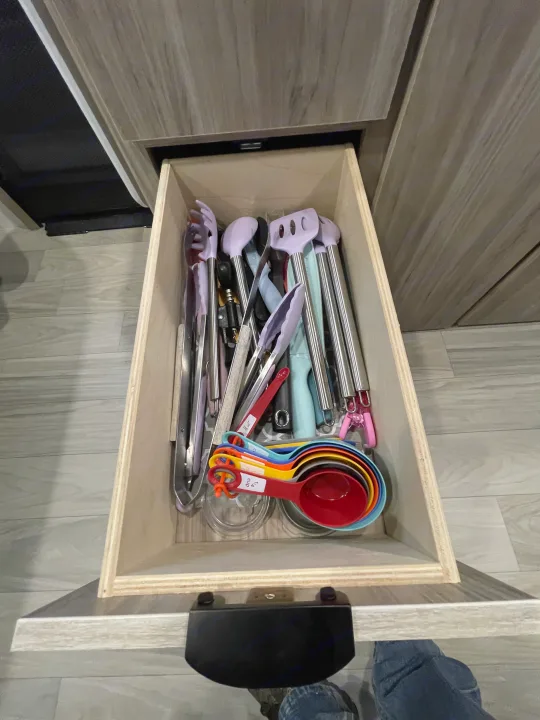 Inside an RV rental kitchen drawer, various cooking utensils and colorful measuring cups are neatly organized, ready for use.. Winnebago M Series 2025