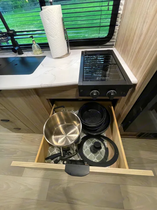 RV rental kitchen: View of a stovetop, sink, and an open drawer neatly storing pots & pans. Efficient, compact cooking setup.. Winnebago M Series 2025