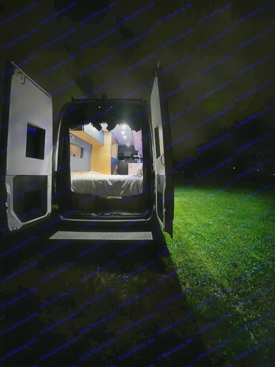Cozy rv rental camper van interior at night with open doors, illuminating grass outside.. Mercedes-Benz Sprinter 2023
