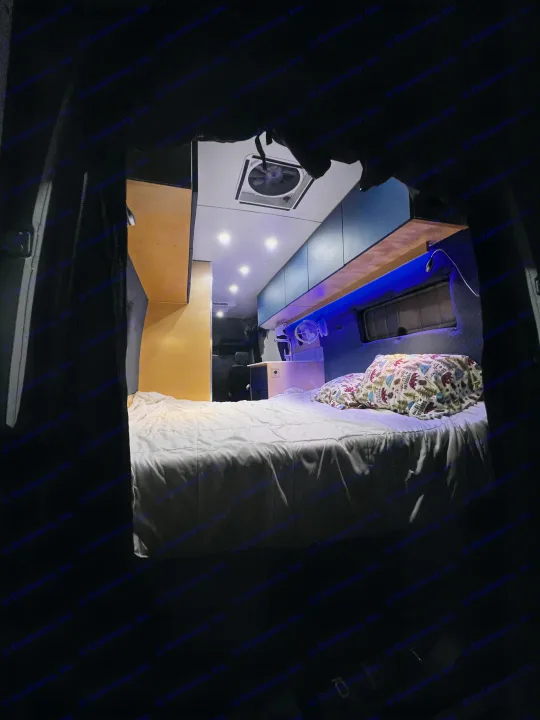 Inside this rv rental, a cozy bed with patterned pillows, blue accent lighting, overhead spotlights, and a ceiling fan create comfort.. Mercedes-Benz Sprinter 2023
