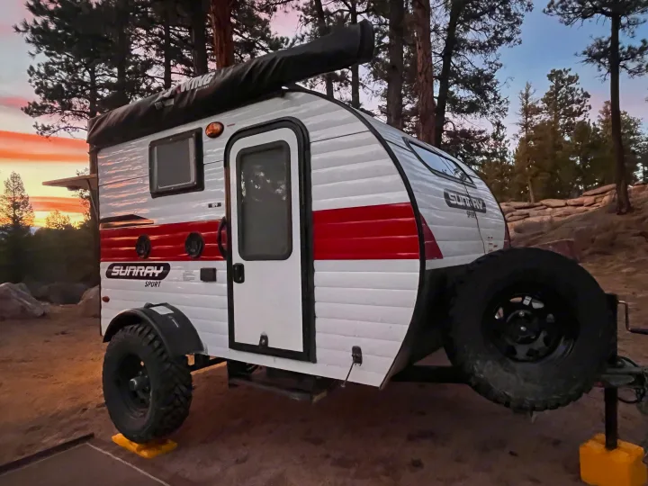 RV rental: a Sunray Sport travel trailer sits among trees at sunset, perfect for outdoor camping adventures.. Sunset Park RV SunRay 2021