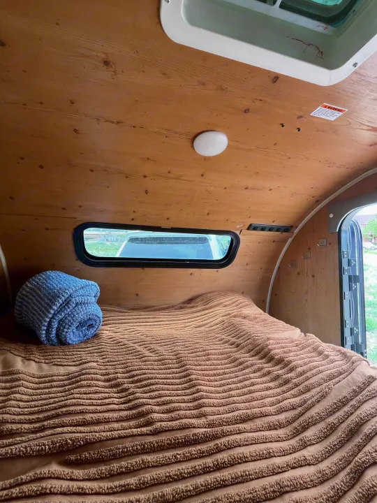 Cozy RV rental interior with wood walls, comfy bed, and blue blanket. Perfect for travel adventures and comfortable nights.. Sunset Park RV SunRay 2021