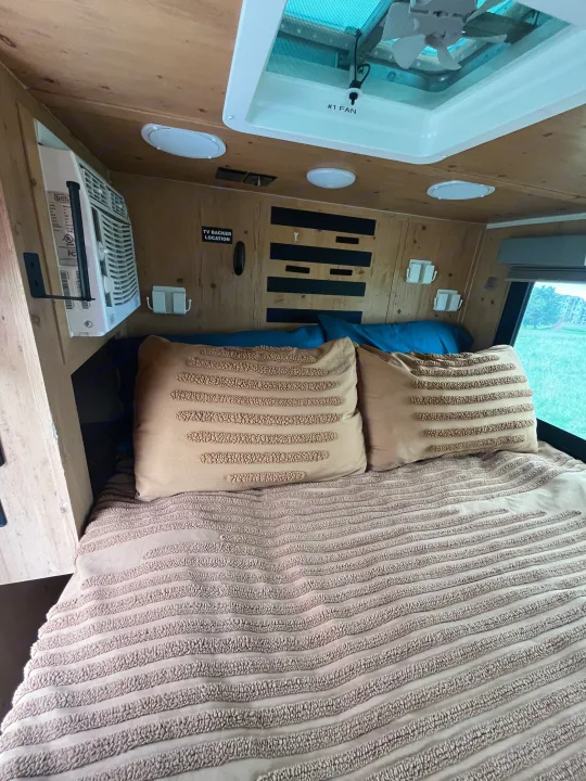 Comfortable RV rental bed with decorative pillows, AC unit, and overhead fan for a cozy night's sleep.. Sunset Park RV SunRay 2021