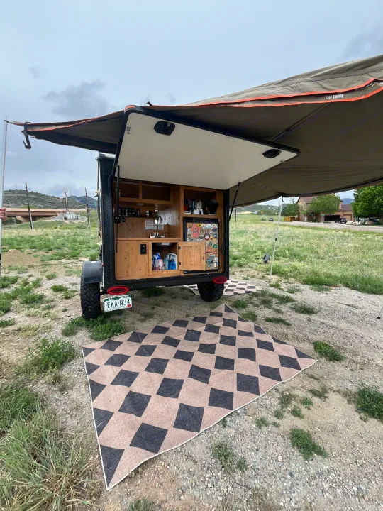 Enjoy your RV rental adventure! Small camper trailer with open kitchen, extended awning, and ground mat for easy outdoor living.. Sunset Park RV SunRay 2021