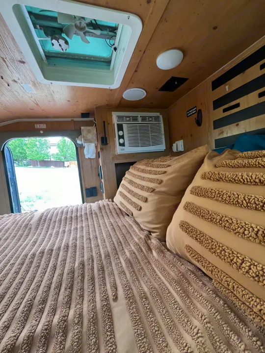 Comfortable RV rental interior: textured bed, AC unit, roof vent, and open door to nature. Perfect for your next trip!. Sunset Park RV SunRay 2021