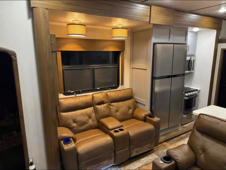 Spacious RV rental interior featuring brown recliners, a large window, and a modern kitchen with stainless steel appliances.. Keystone Fuzion 2020