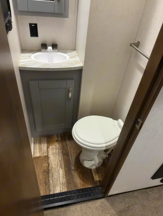 RV rental bathroom: A compact space with a white sink, gray vanity cabinet, and white toilet on a wood-look floor.. Keystone Fuzion 2020