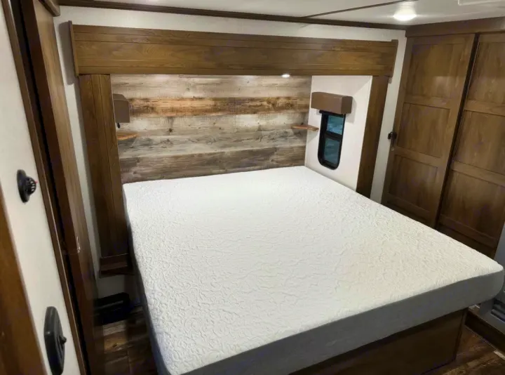 Comfortable RV rental bedroom featuring a large bed, rustic wood headboard, window, and wardrobes, perfect for travel.. Keystone Fuzion 2020