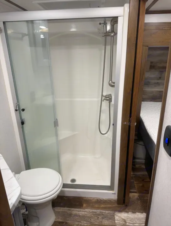Inside an RV rental, this compact bathroom features a white toilet, a modern shower stall with sliding glass doors, and durable wood-look flooring.. Keystone Fuzion 2020
