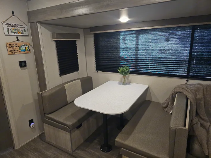 Experience comfort in this RV rental's dinette, complete with cozy bench seating, a clean white table, and privacy blinds.. Forest River Aurora Aurora 2026