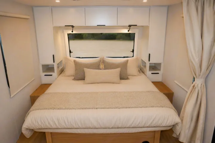 Cozy, modern RV rental bedroom features a comfortable bed, built-in storage, plush bedding, and a scenic window view for travel.. Winnebago Thrive 2026