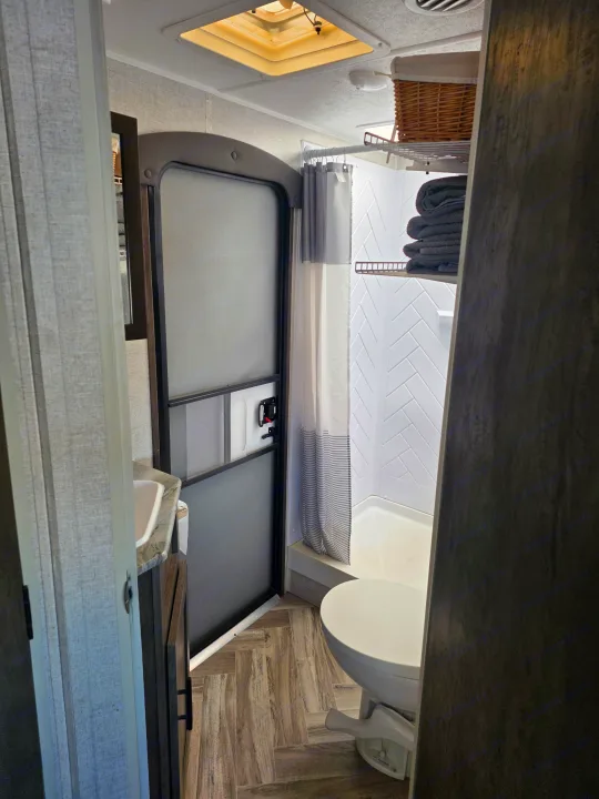 RV rental bathroom features a compact toilet, shower with herringbone tile, and vanity. Ready for your travels!. Forest River Wildwood 2021