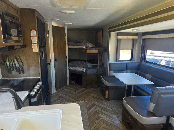 Inside an RV rental: full kitchen with microwave, U-shaped dinette, and bunk beds. Comfortable and ready for travel.. Forest River Wildwood 2021