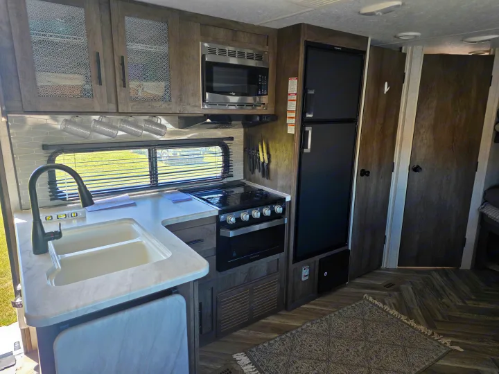 Spacious, modern rv rental kitchen featuring a double sink, Dometic fridge, Furrion stove/oven, microwave, and stylish wood-look flooring.. Forest River Wildwood 2021