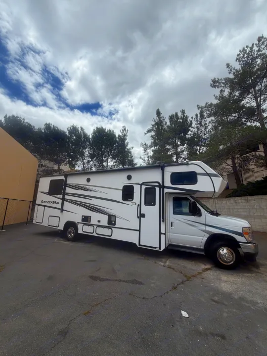 White Sunseeker Class C RV rental, parked on asphalt. Perfect for your next road trip adventure under a cloudy sky.. Forest River Sunseeker LE 2024