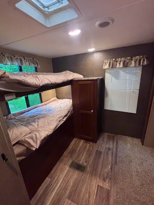 RV rental bunk beds: upper and lower bunks, windows, skylight, and storage cabinet, showcasing a cozy sleeping area.. Keystone RV Passport Grand Touring 2016