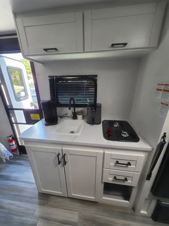 This modern RV rental kitchen features white shaker cabinets, sink, gas stovetop, air fryer, and coffee maker.. Jayco Jayco 2026