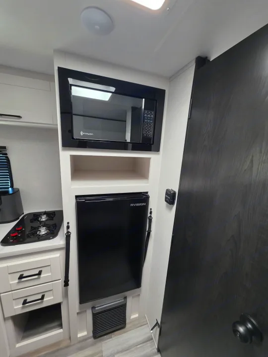 RV rental kitchen: compact space with microwave, fridge, two-burner stovetop, white drawers, and a dark door.. Jayco Jayco 2026