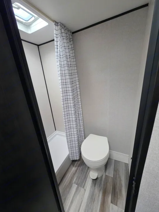Compact RV rental bathroom featuring a toilet, shower with plaid curtain, and skylight. A clean, practical space for travel.. Jayco Jayco 2026