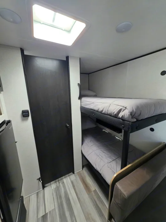 Cozy RV rental interior showcasing bunk beds with grey bedding, a skylight, wood-look flooring, and a small sofa for guests.. Jayco Jayco 2026