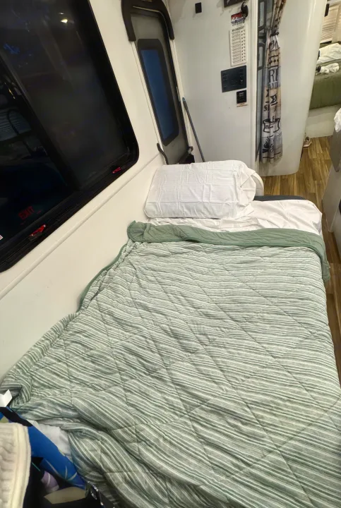 RV rental bedroom with a bed featuring striped green & white bedding, an exit window, and a wall-mounted RV checklist.. Forest River Coachmen Freelander 2017