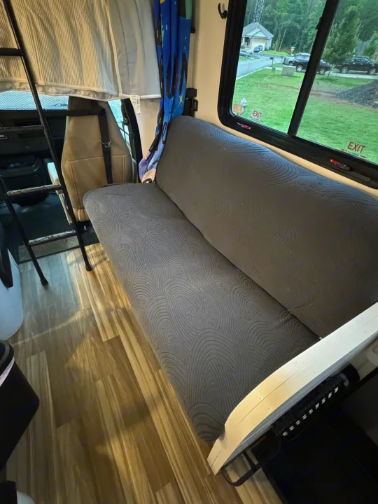 RV rental interior: gray patterned sofa, laminate floor, bunk access ladder, and a window view of homes outside.. Forest River Coachmen Freelander 2017