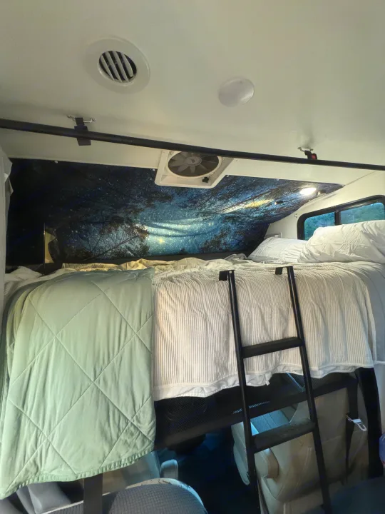RV rental interior: A cozy bunk bed with a ladder, starry night mural, and comfortable bedding for a snug travel experience.. Forest River Coachmen Freelander 2017