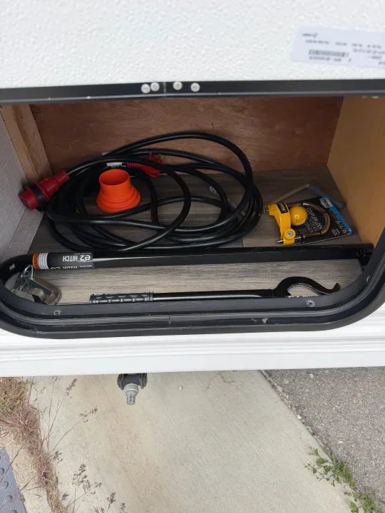 RV rental storage with a coiled power cord, e2 hitch bar, and Reese coupler lock for secure towing and hookup.. Highland Ridge RV Open Range 2023