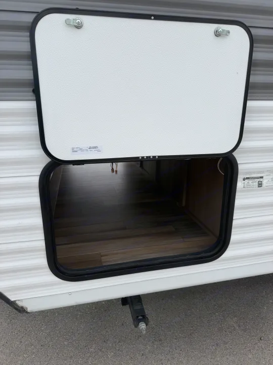 Open exterior storage compartment on an RV rental, revealing a wood-look floor. A leveling jack is seen below.. Highland Ridge RV Open Range 2023