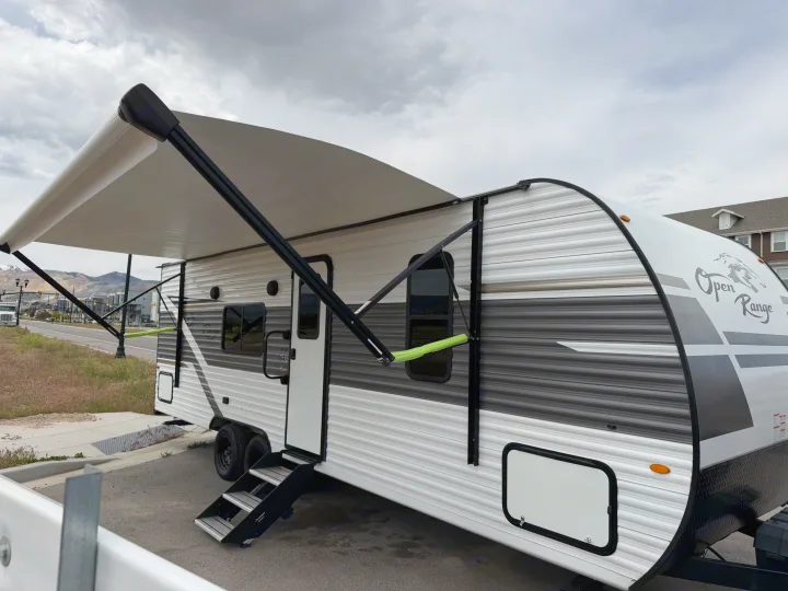 Open Range RV rental: A white & grey travel trailer with an extended awning, parked outside on a cloudy day.. Highland Ridge RV Open Range 2023