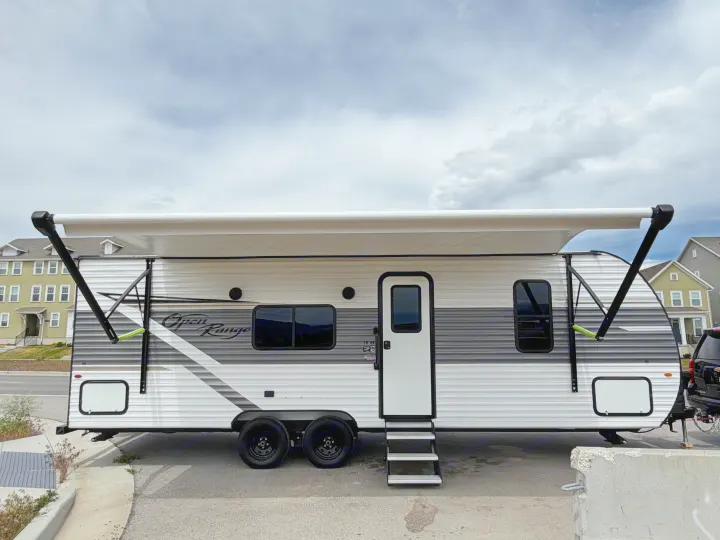 A white and gray Open Range travel trailer rv rental, with an extended awning, parked outside under a cloudy sky.. Highland Ridge RV Open Range 2023