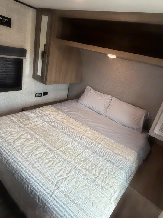Cozy RV rental bedroom with a striped and quilted bed, overhead storage, and bedside charging, perfect for comfortable journeys.. Highland Ridge RV Open Range 2023
