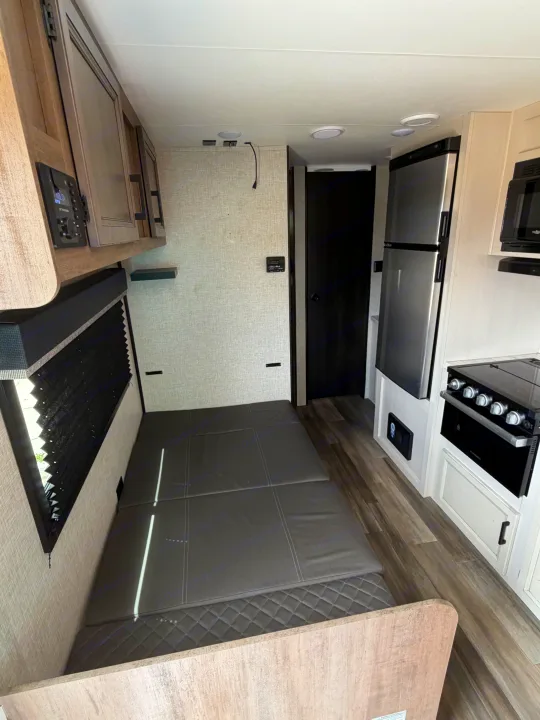 RV rental interior: compact kitchen (fridge, stove, microwave) and bed/seating area, perfect for travel.. Highland Ridge RV Open Range 2023