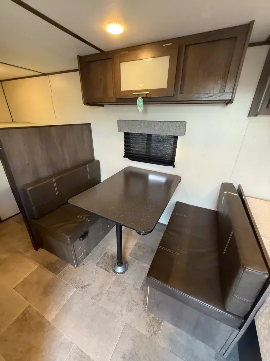 RV rental interior: a functional dinette with dark brown bench seating, a table, and overhead cabinets for storage.. Coleman 17B Dutchmen 2022