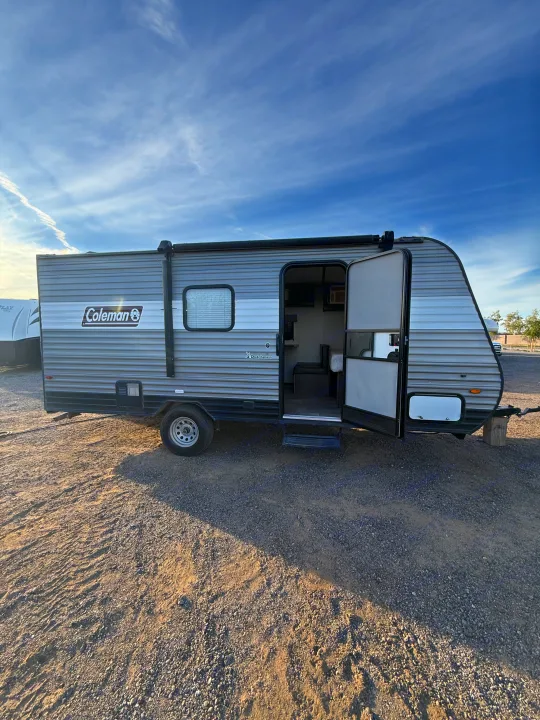 This Coleman travel trailer RV rental, with its door open, is parked on a gravel lot, ready for your next camping adventure.. Coleman 17B Dutchmen 2022