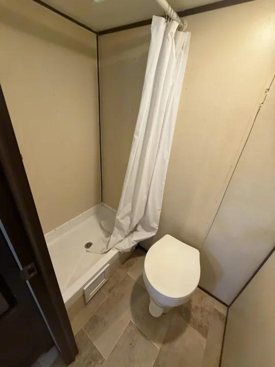 Compact RV rental bathroom with shower stall, white curtain, & toilet. Gray tiled floor.. Coleman 17B Dutchmen 2022